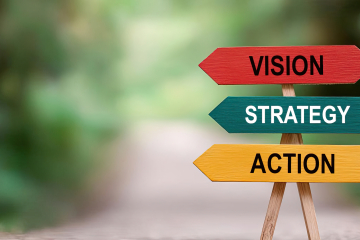 Three wooden arrow signs in red, teal, and yellow reading Vision, Strategy, and Action on a trail.