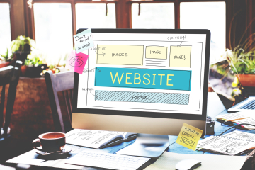 Monitor shows a website wireframe layout on a cluttered desk with sticky notes; plants and a notebook in the background.