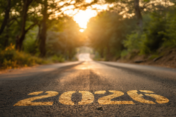 Close-up view of a road with a large painted speed limit marking on the asphalt, sunlit trees in the background at sunset.